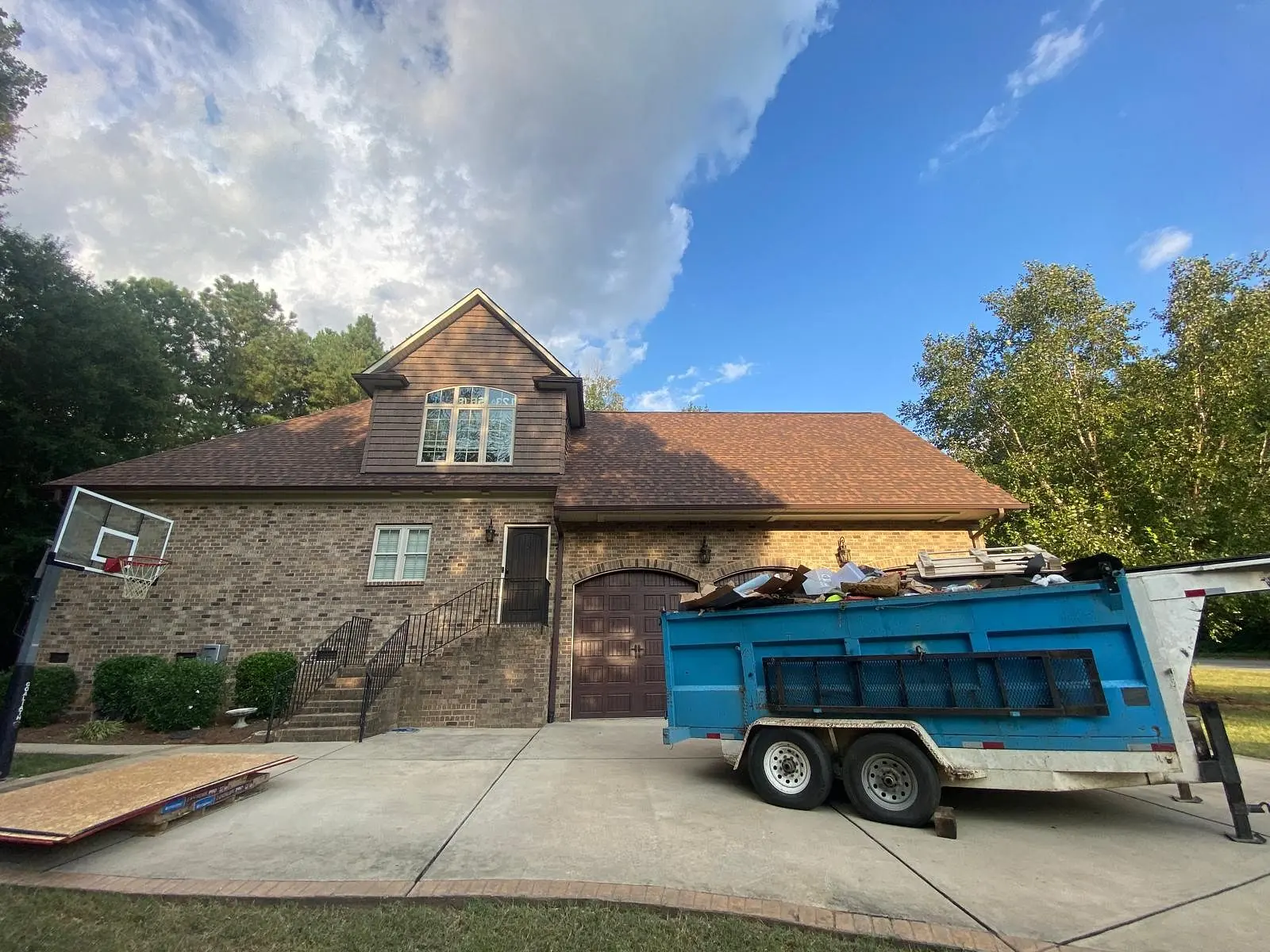 Brick home with new brown shingles and a debris trailer