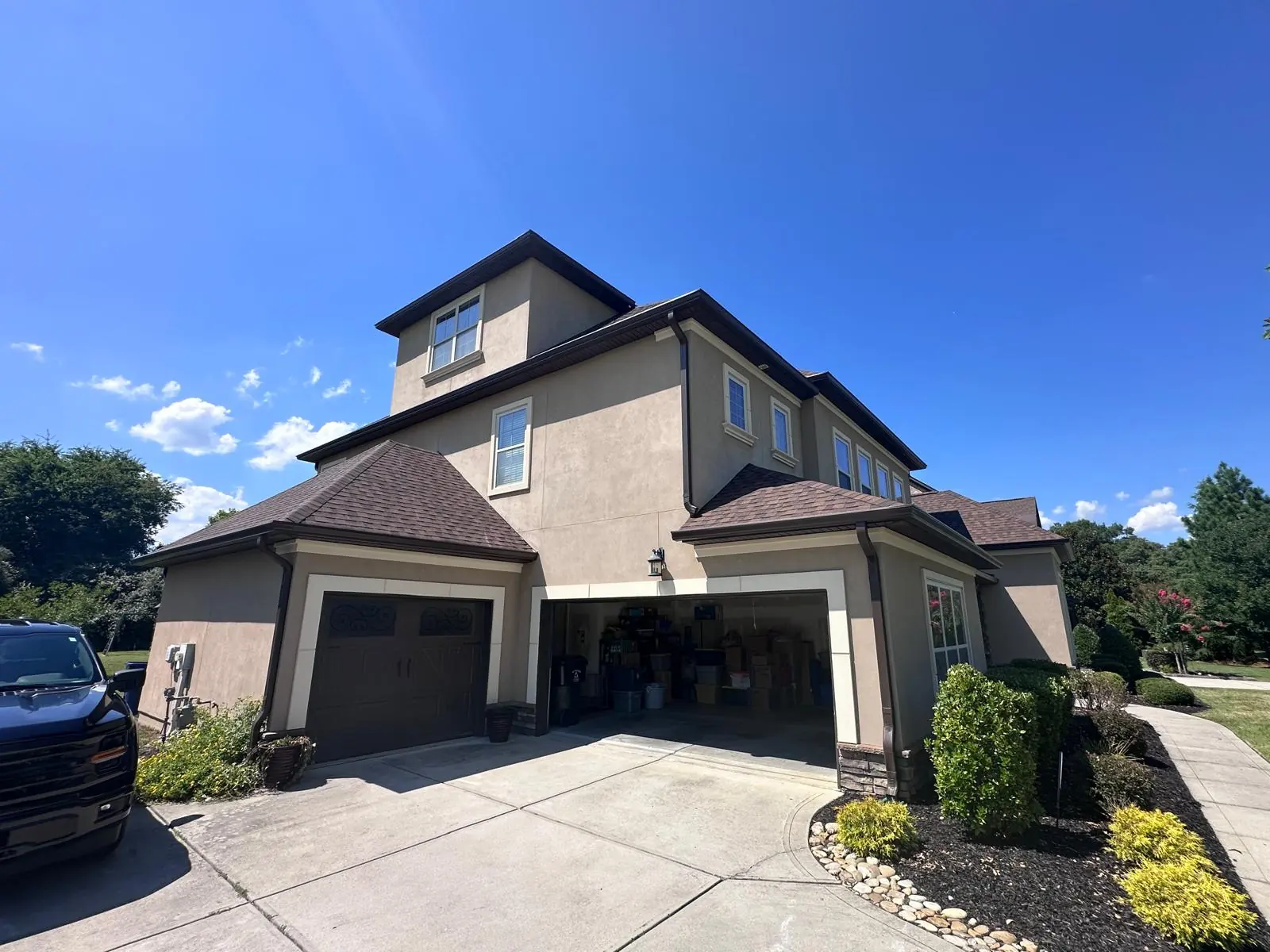 Side of a stucco home with new shingles and matching brown gutters