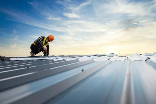 Roofer installing metal panels on a commercial roof at sunset