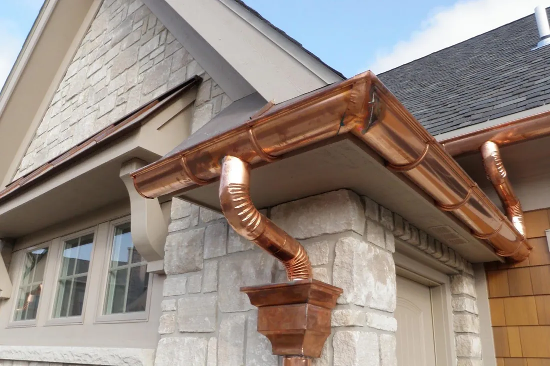 Copper half-round gutters and downspouts on a stone home